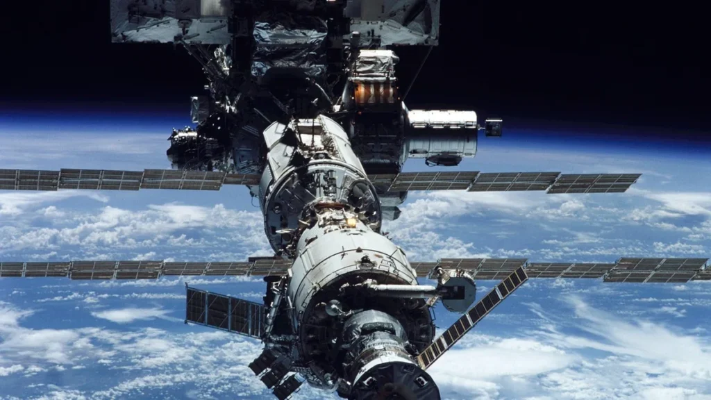 The International Space Station orbits above a cloud-covered blue Earth, displaying its solar arrays and modules.