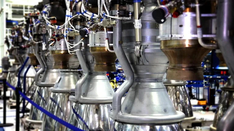 Row of metallic rocket engines with copper-colored nozzles and complex wiring in an assembly facility.