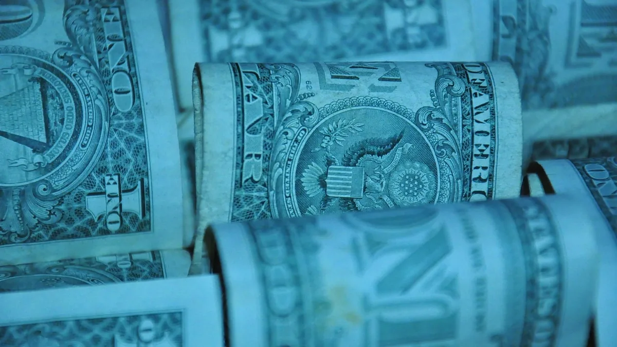Close-up of rolled-up US dollar bills under a blue tint, symbolizing finance and massive monetary sums.