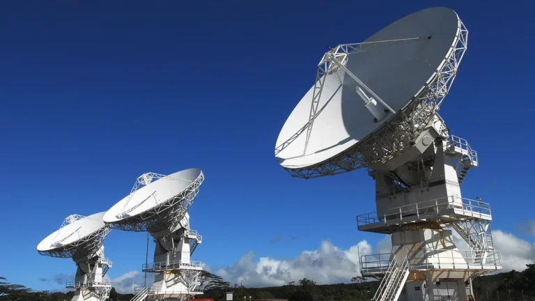 Large white satellite dishes stand against a clear blue sky, symbolizing space-to-earth ground connectivity.