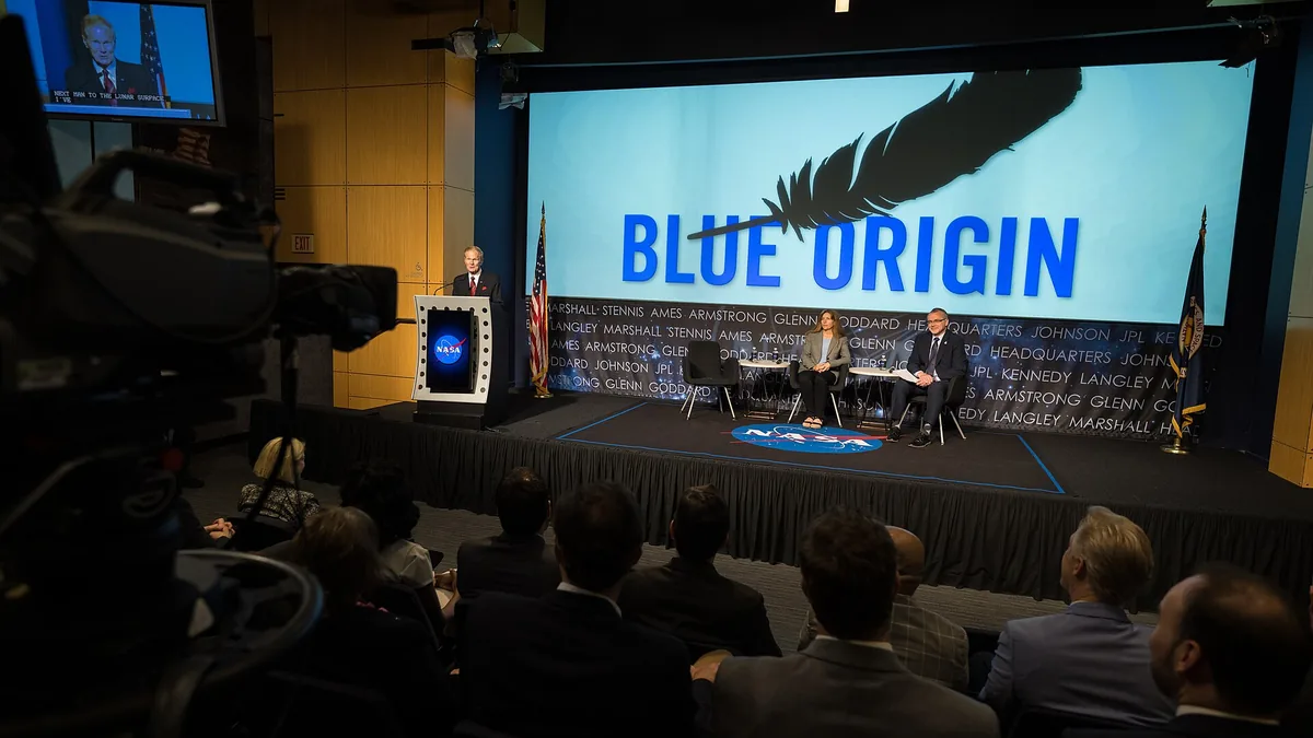 A presentation stage featuring a large Blue Origin logo on a screen and a NASA logo on the podium.