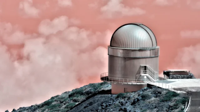 Silver observatory dome perched on a rocky ridge under a surreal pink cloudy sky.