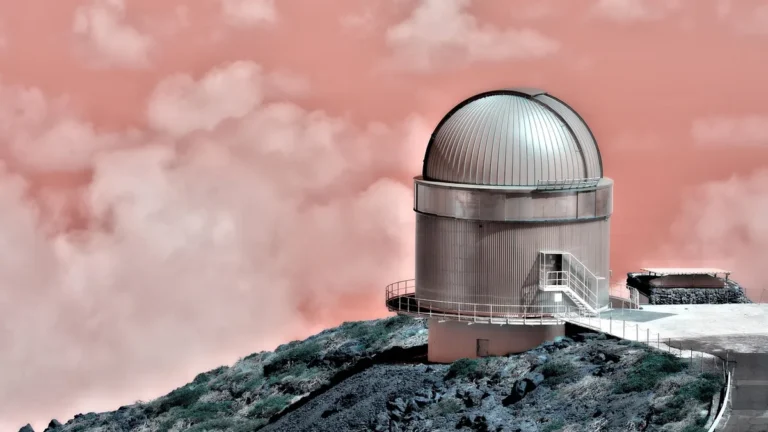 Silver observatory dome perched on a rocky ridge under a surreal pink cloudy sky.