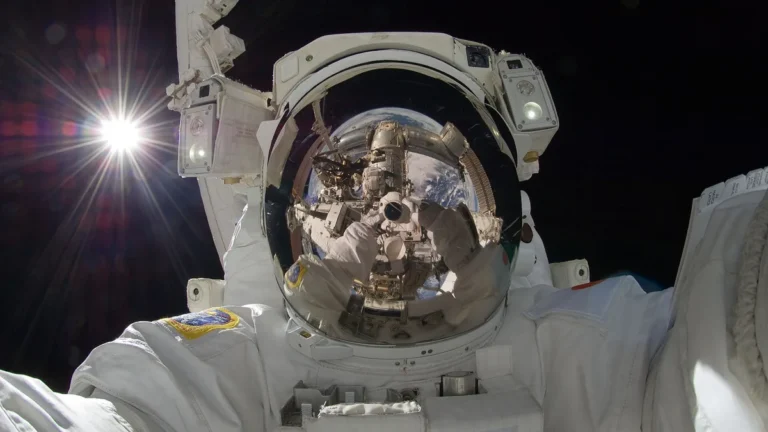 Astronaut selfie showing the sun flaring in the background and the space station reflected in the visor.