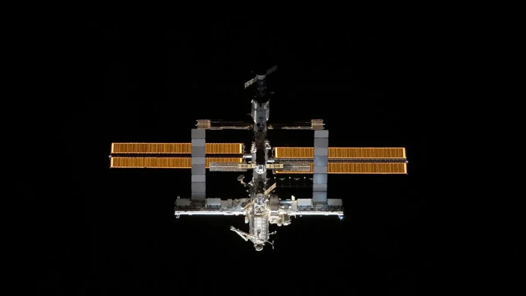 The International Space Station glowing against the deep blackness of space, solar arrays illuminated.
