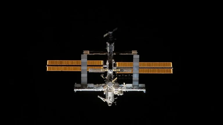 The International Space Station glowing against the deep blackness of space, solar arrays illuminated.