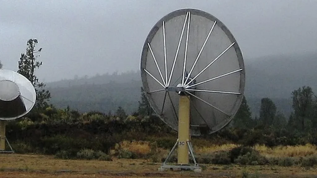 A large radio telescope dish stands against a misty, forested landscape, key for radio astronomical observations.