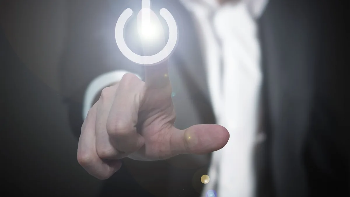 Hand in a suit touching a glowing white power symbol, representing system activation or reboot.