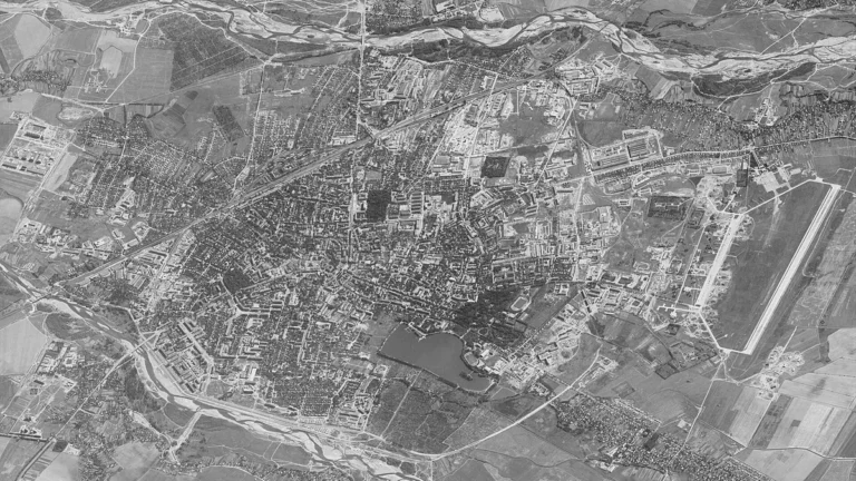 High-resolution black-and-white satellite imagery showing a city layout with a large airfield and surrounding rivers.