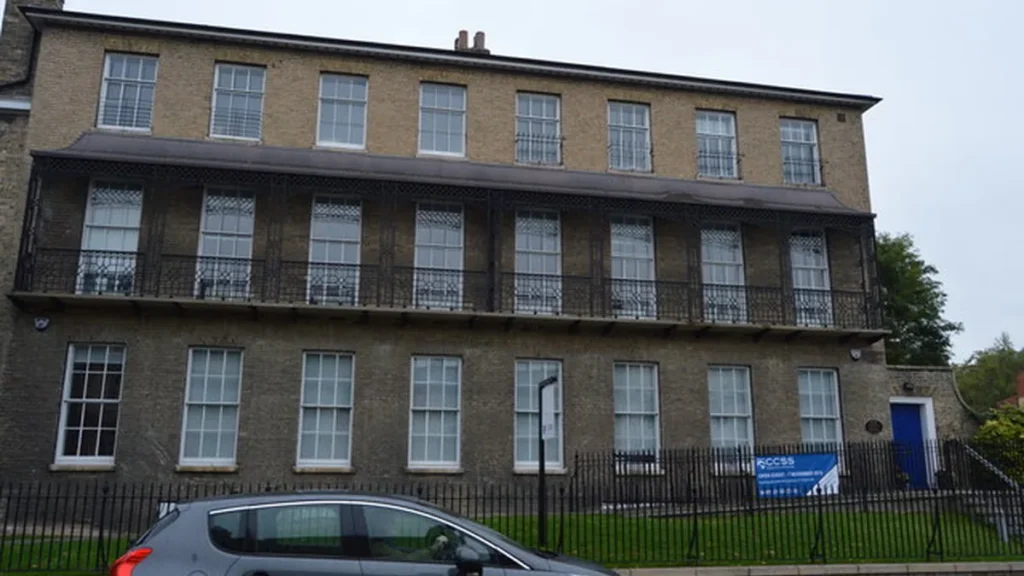 Brick building of Cambridge university with a blue CCSS banner behind a black metal railing.
