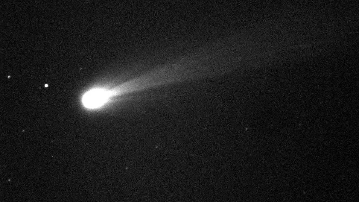 A bright comet with a long tail streaking across a dark, starry sky in black and white.