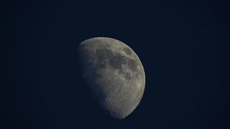 Detailed view of a gibbous moon showing craters and maria against a dark blue sky.
