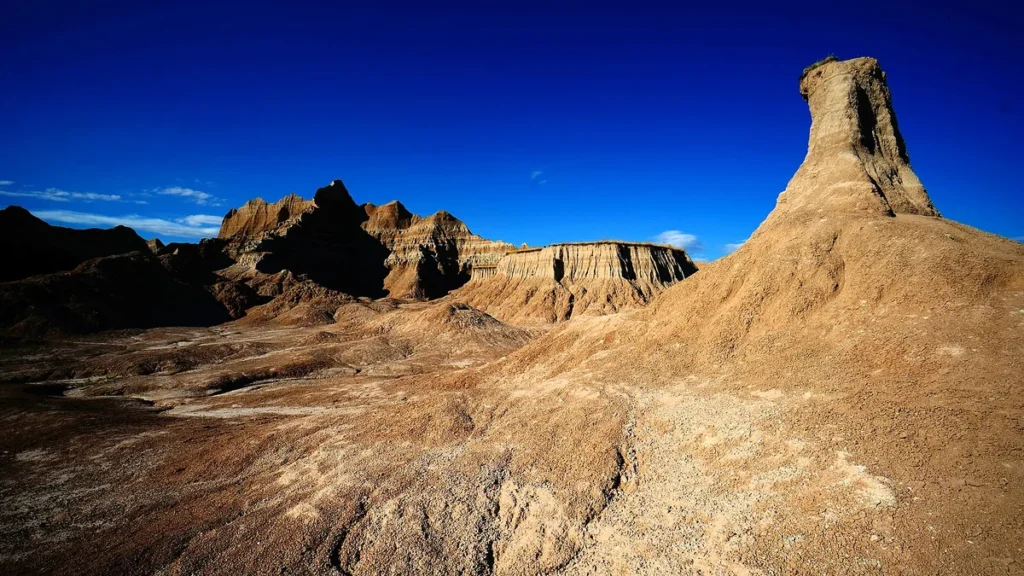 Barren badlands landscape with a tall rock spire under a vibrant blue sky.