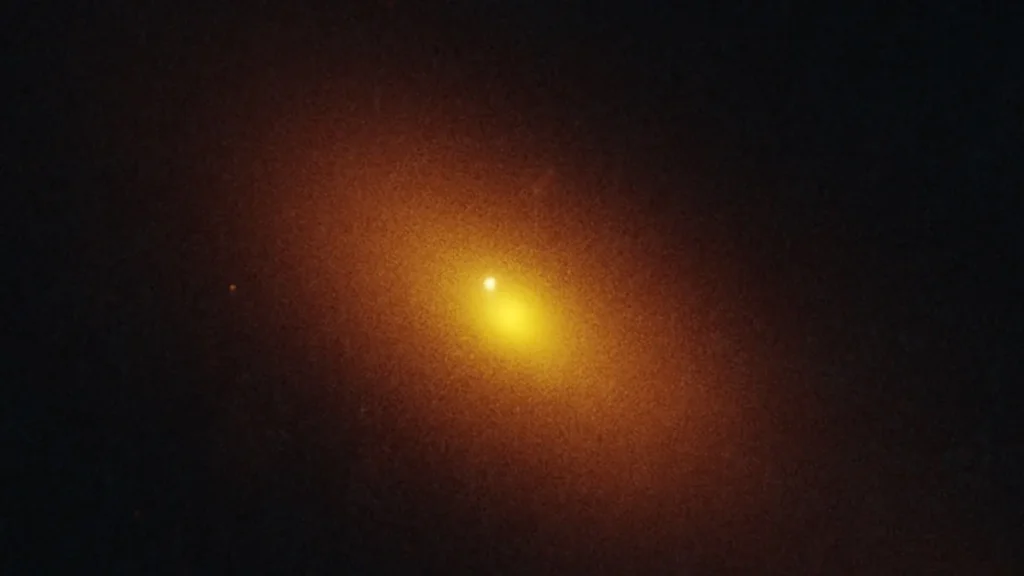 A glowing orange galaxy with a bright white point source offset from the yellow core, representing a tidal disruption.