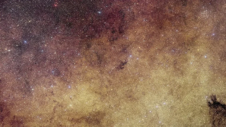 A vibrant, colorful star field filled with golden and reddish cosmic dust and countless bright stars.