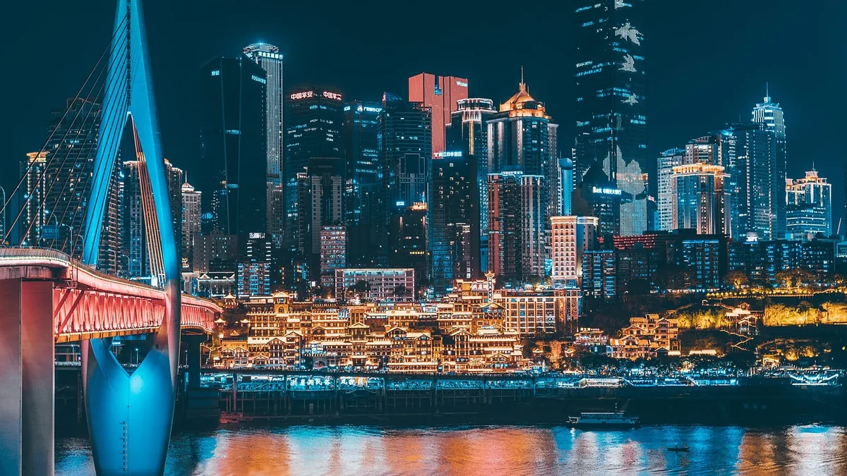 A Chinese city skyline at night, featuring glowing skyscrapers, traditional buildings, and a colorful blue bridge over the