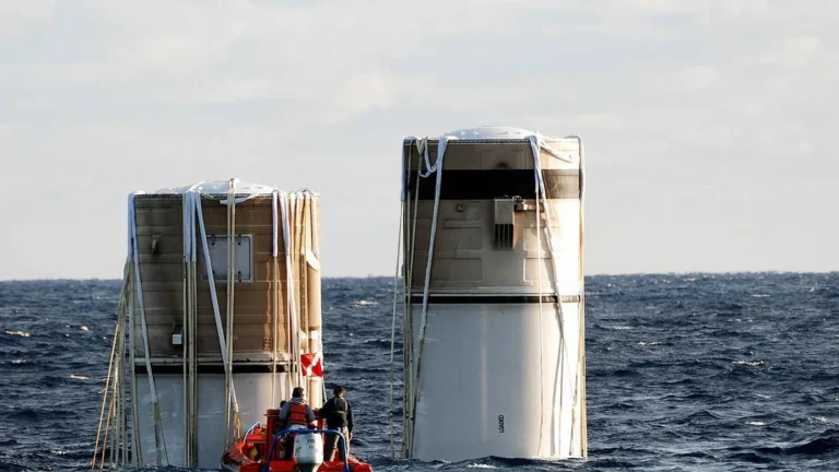 Recovered rocket booster segments float vertically in the ocean with a small recovery boat nearby.