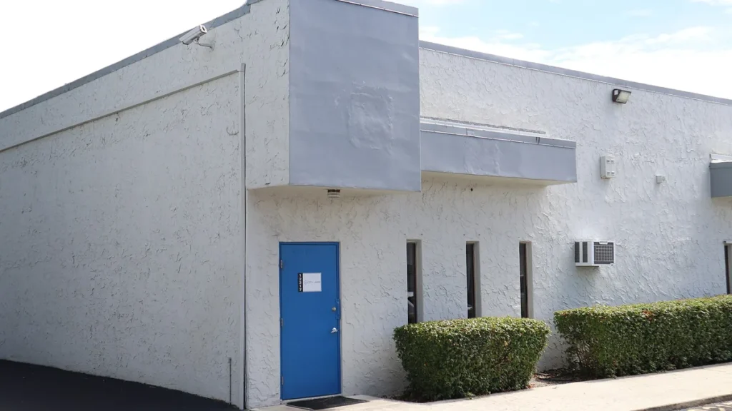 The exterior of the City Labs facility, featuring a white stucco wall, a blue door, and green hedges.