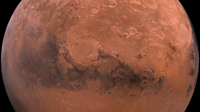 A detailed view of the reddish-orange, cratered surface of planet Mars against a black space background.