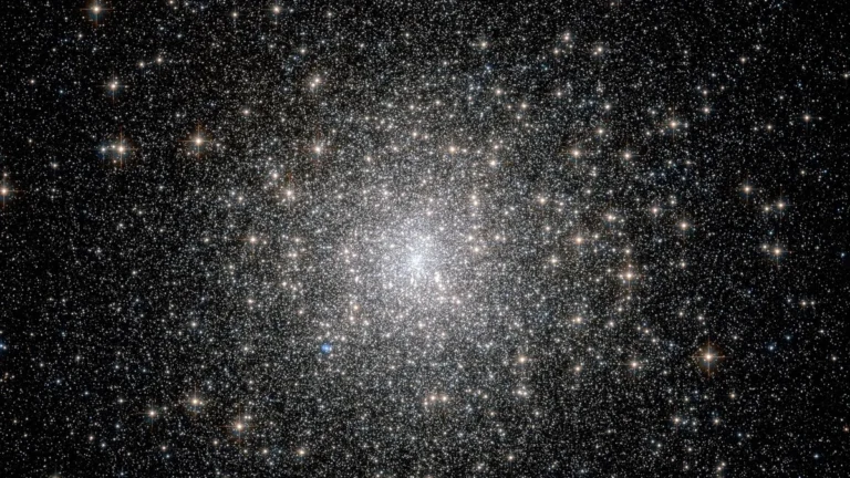 A dense, glittering cluster of thousands of stars against a dark cosmic background, with a bright blue star nearby.