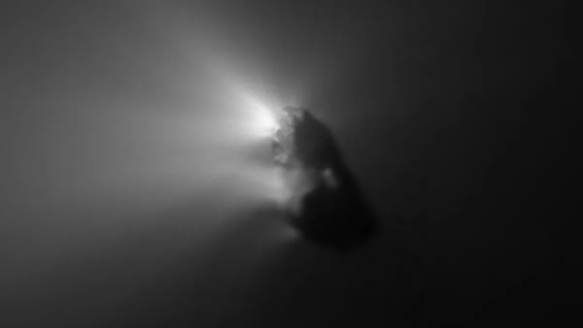 A dark comet nucleus emitting a bright jet of light against the dark void of space.