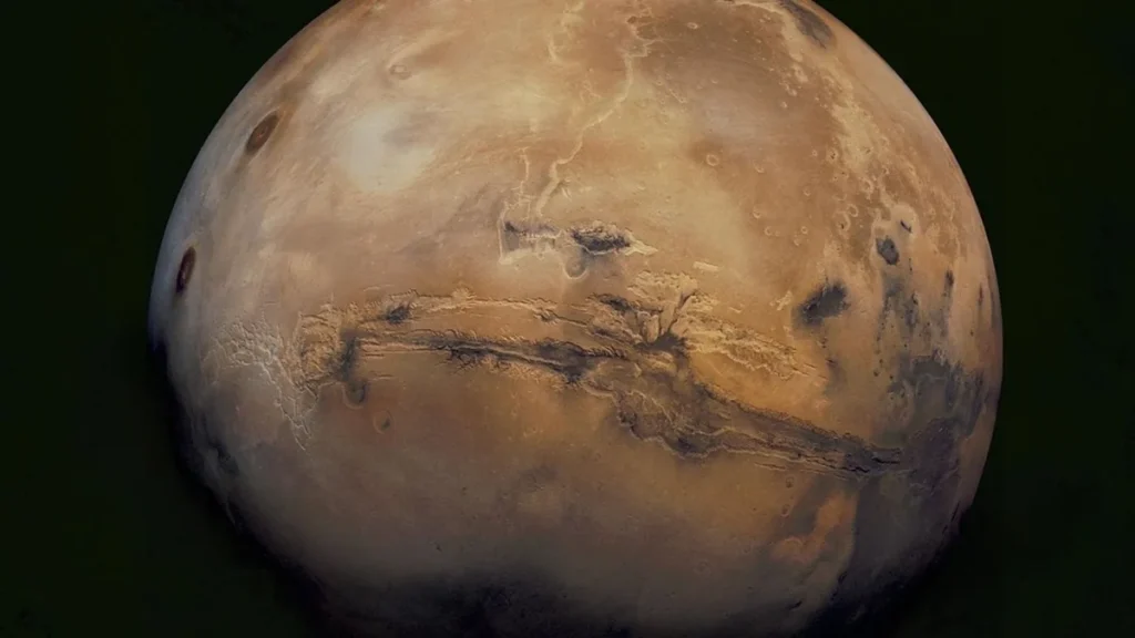 Global view of the rusty-red planet Mars showing the prominent Valles Marineris canyon system stretching across its surface.