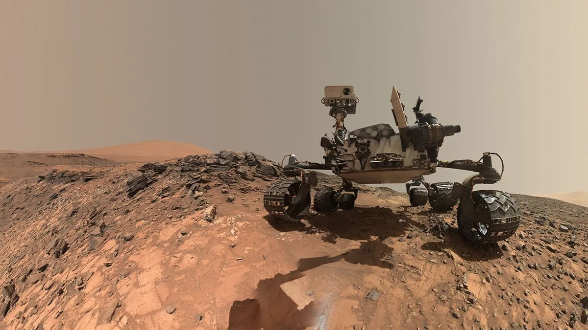 Self-portrait of NASA's Curiosity rover on a rocky Martian ridge under a dusty orange sky.