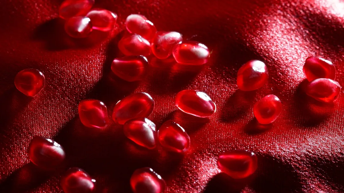 Close-up of shiny red pomegranate seeds scattered on red satin fabric, resembling red garnet gems.