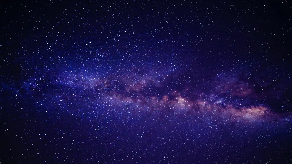 A vibrant purple and blue band of the Milky Way galaxy stretches across a star-filled dark night sky.
