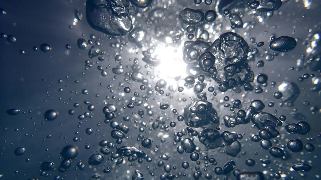 Shiny bubbles floating in dark liquid, backlit by a bright central light source.