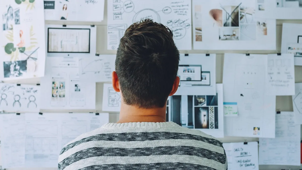 Man from behind in striped sweater looking at a wall of design sketches and strategy diagrams.