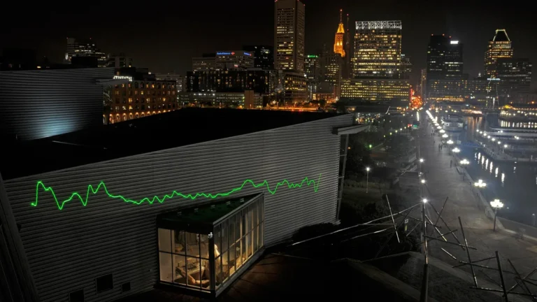Green spectrum-like line projected on a modern building at night with a city skyline in the background.