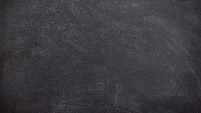 A dark, textured chalkboard surface with faint white smudges.