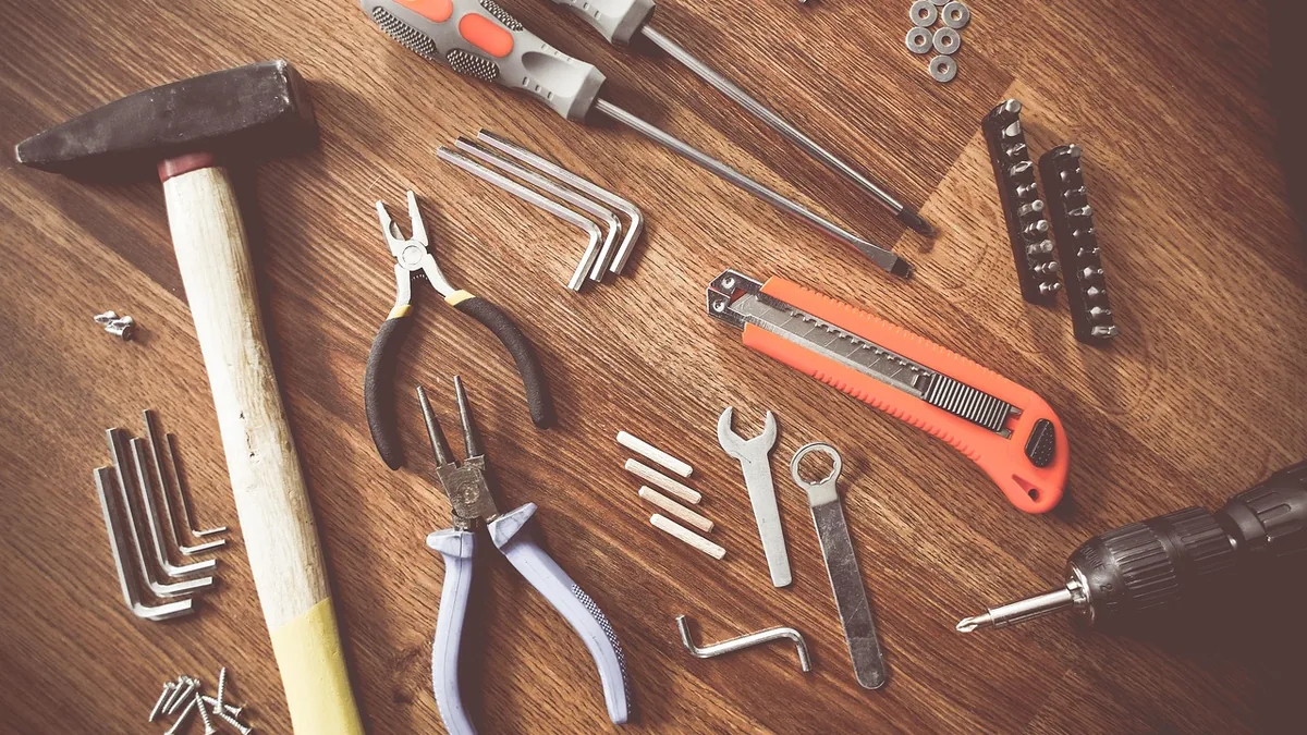 Assorted hand tools, including a drill, hammer, and pliers, arranged on a wooden table.