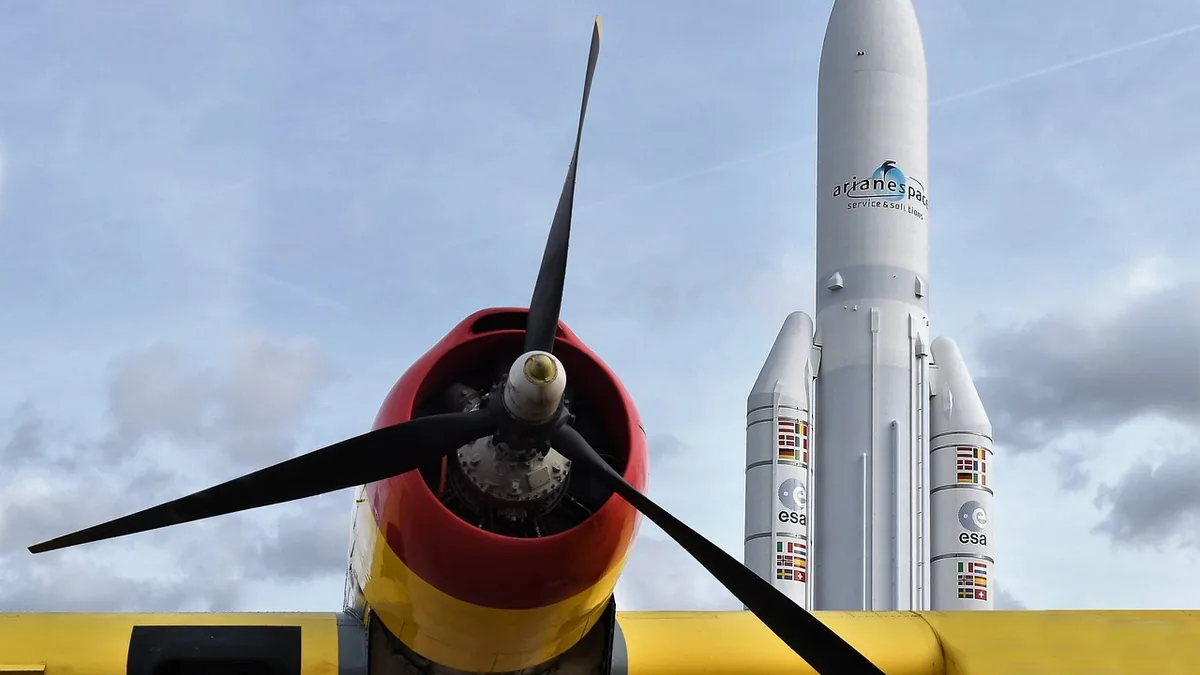 Propeller plane engine in foreground, ESA Ariane 6 rocket model in background under cloudy sky.