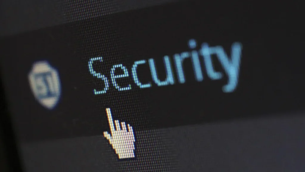 Pixelated cursor pointing at the word 'Security' with a shield icon on a dark digital screen.