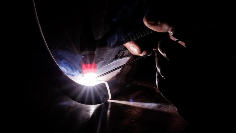 Close-up of precision welding on a metal pipe, with a brilliant bright light flare and smoke in darkness.