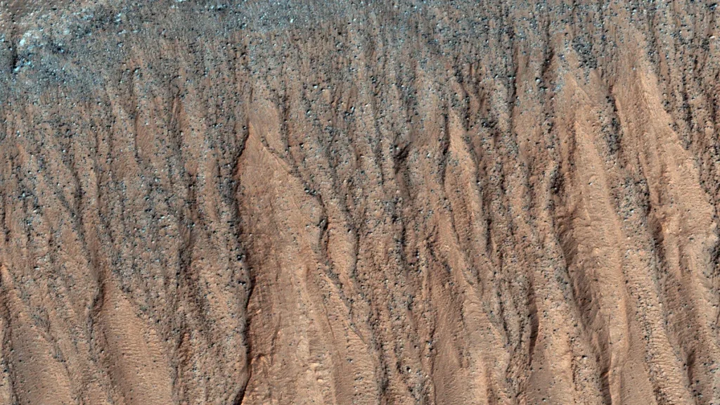 High-resolution view of Martian gullies on a steep slope, showing bluish carbon dioxide frost near the top.