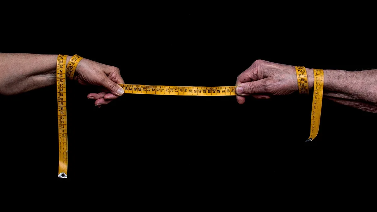 Hands holding a yellow measuring tape stretched horizontally against a black background, showing precise measurements.