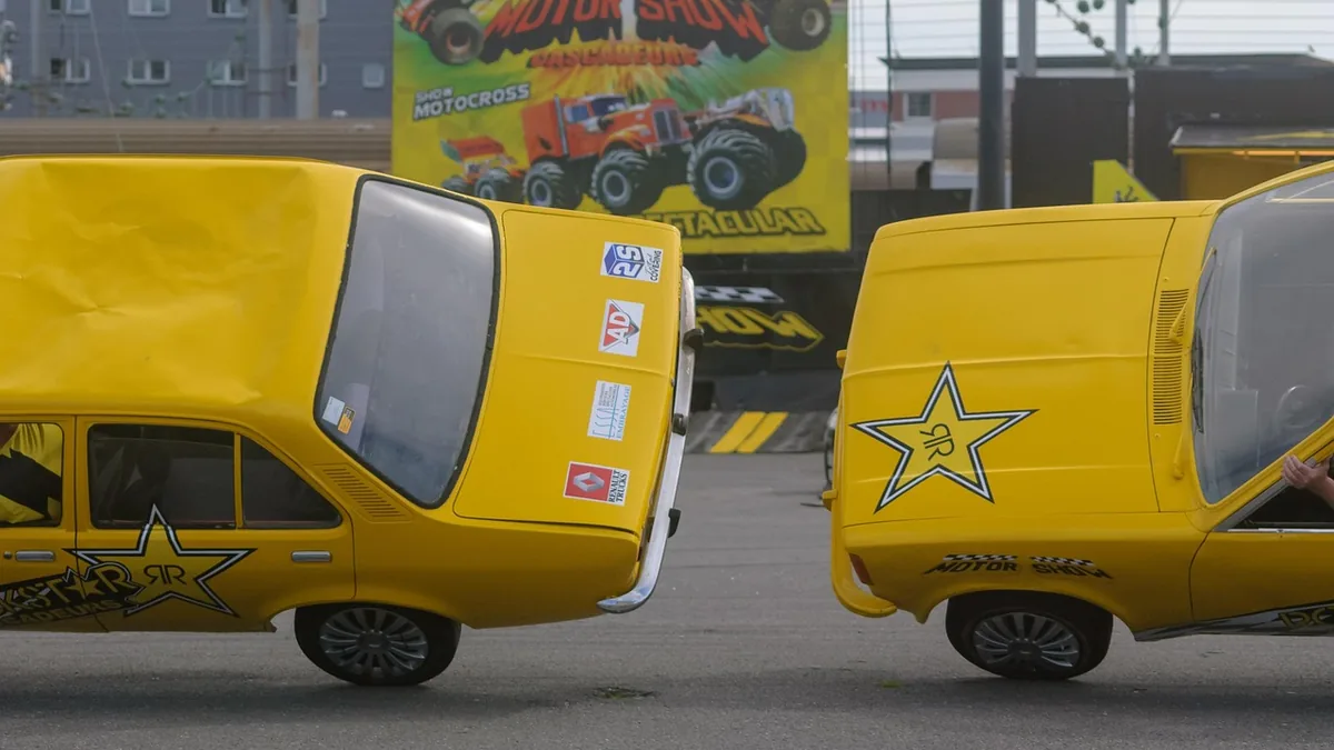 Yellow cars with star logos crash into each other during a stunt show, with a colorful motor show billboard in the
