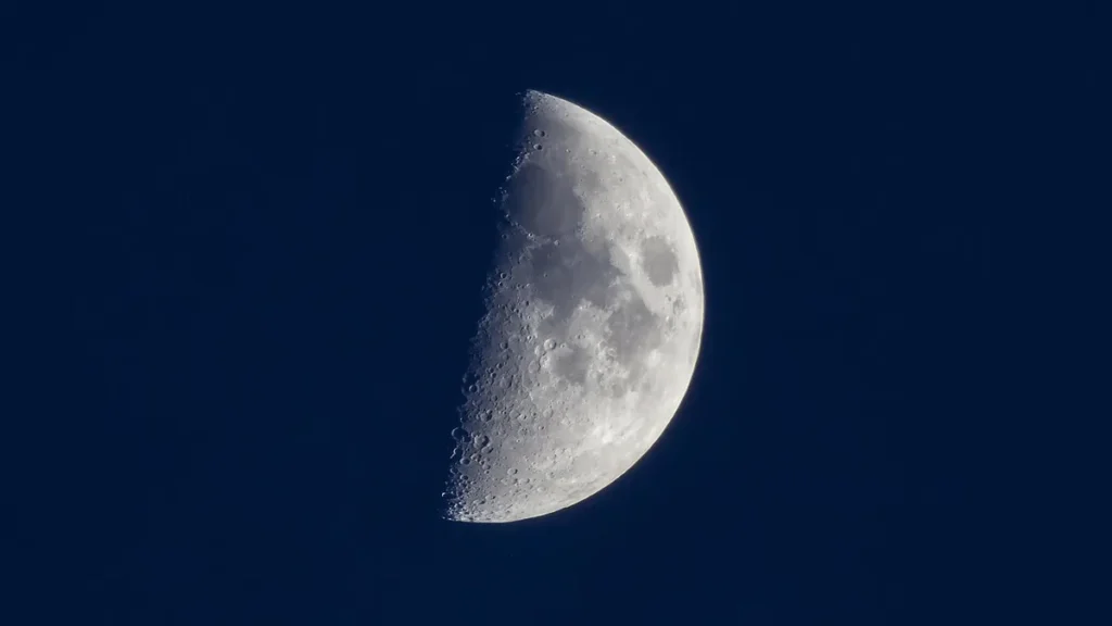A detailed view of the moon's craters along the terminator line against a deep blue sky.
