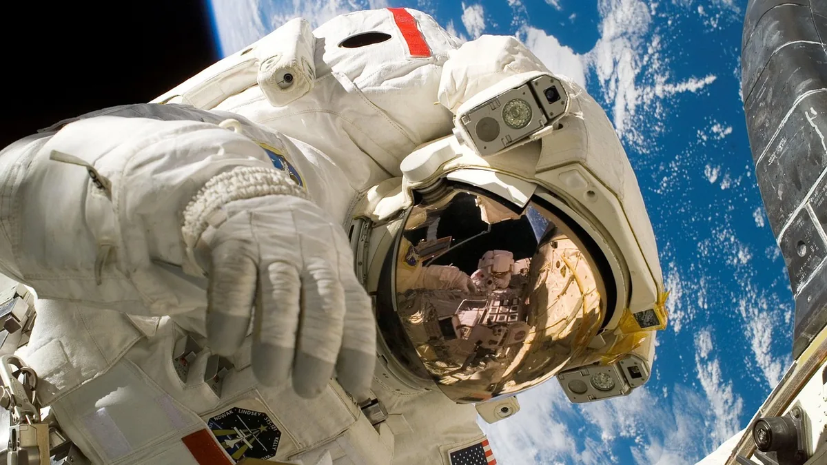 A close-up of an astronaut in a spacesuit with Earth and a visor reflection in space.