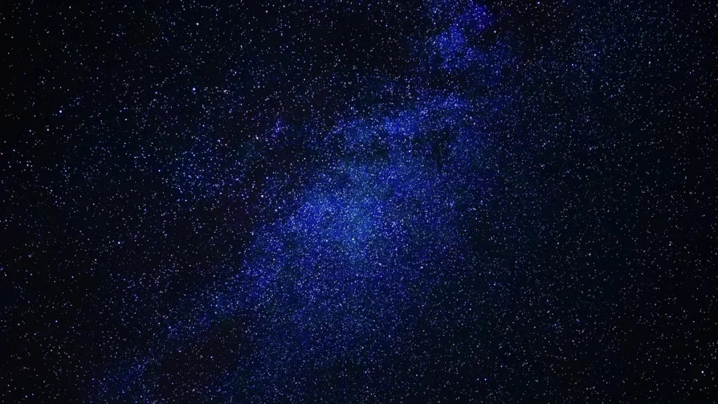 A vibrant blue band of the Milky Way stretches across a star-filled dark night sky.