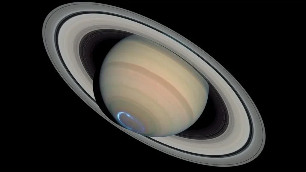 Saturn with its majestic rings and a glowing blue aurora at the pole against black space.
