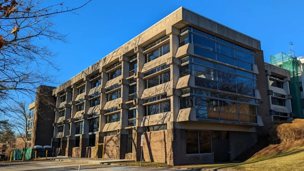 Brutalist concrete academic building under a clear blue sky, representing a scientific research facility.