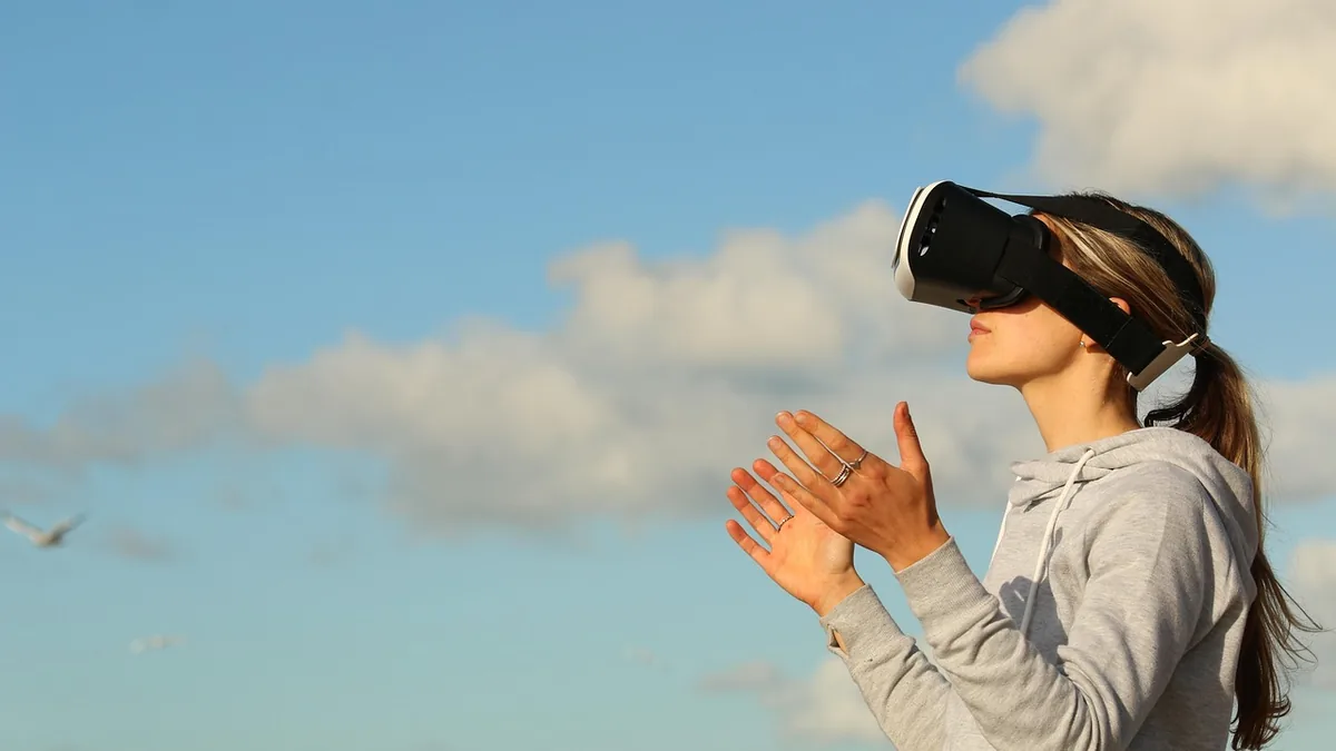 Woman in profile wearing a VR headset against a blue sky with clouds, hands raised in interaction.