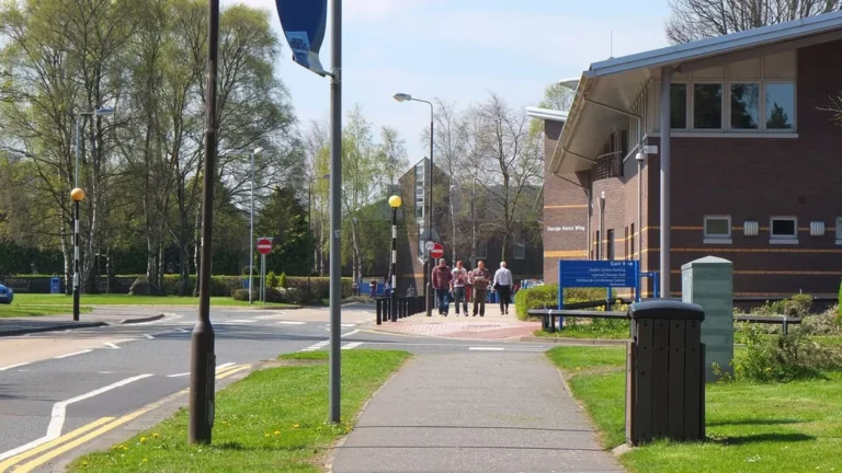 View of the George Heriot Wing at Heriot-Watt University campus with a pathway and people walking on a sunny day.