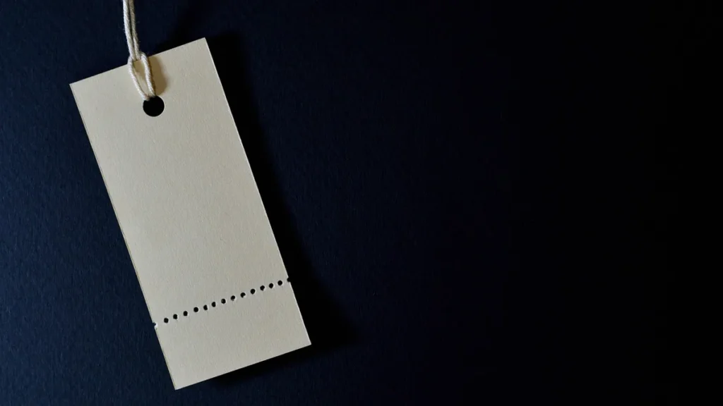 Blank beige price tag hanging on a string against a dark blue textured background.