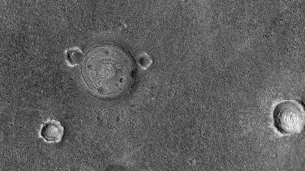 Black and white satellite view of the Martian surface featuring impact craters and polygonal terrain patterns.