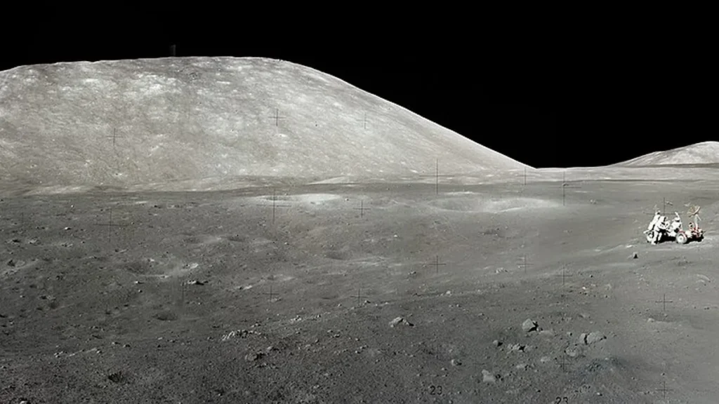Monochrome lunar landscape with a large hill and a small rover with astronauts on the right.